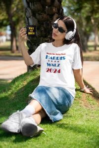 Young woman with headphones in the park wearing a white Harris/Walz t-hirt